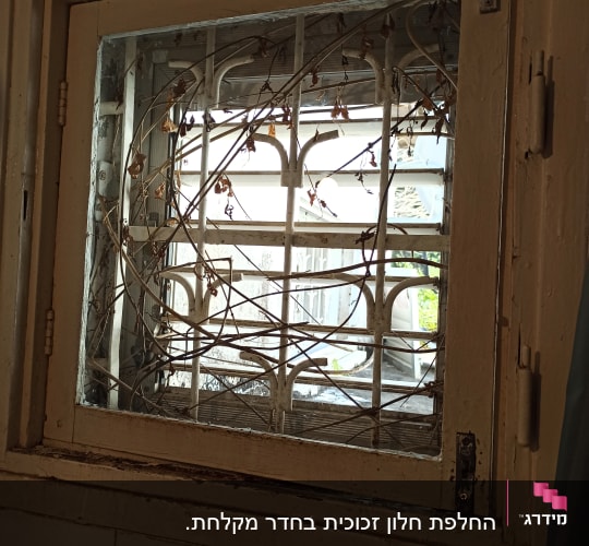חלון עץ ישן עם סורגים וענפים יבשים על קיר אריחים